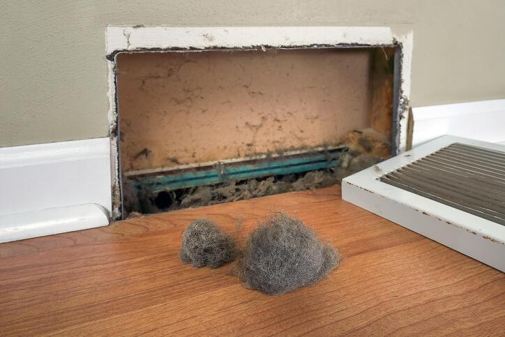 An air vent with the metal grate removed and balls of dust and debris pulled out of the air duct. 