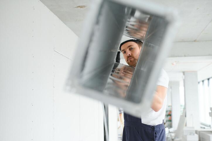 Image of a man in work clothes looking through a removed air duct that is completely clean.