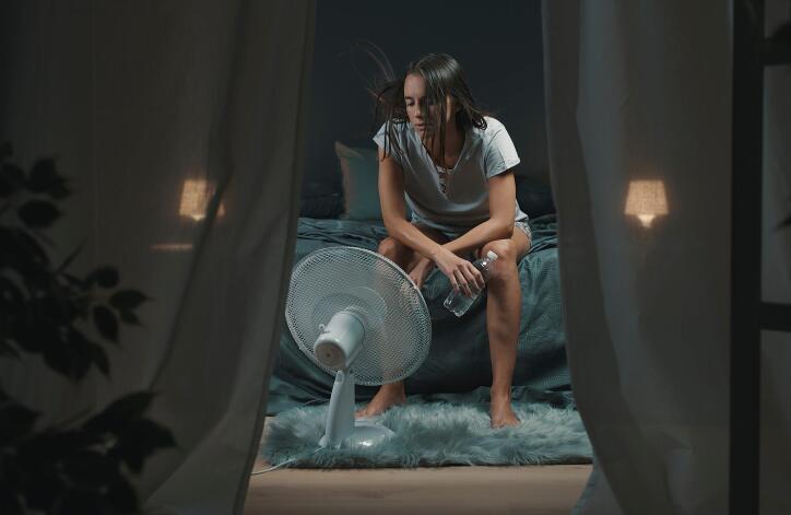 A woman sitting in front of fan. The AC isn't working as efficiently as it could with an air duct cleaning by Scrubber Ducts.